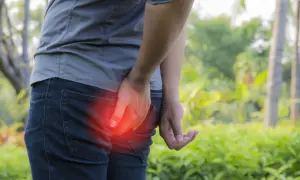Person tenant sa fesse, rougeur indiquant une douleur. Recherche d'un furoncle fessier traitement naturel.