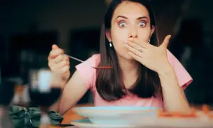 Femme surprise avec une cuillère de soupe, main sur la bouche, comme si elle avait le hoquet persistant.