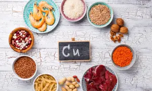 Assiette de crevettes, bols de riz, lentilles, haricots, pâtes, cacahuètes, noix, foie et un tableau noir avec "Cu" pour les cuivre bienfaits.