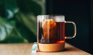 Un moment de détente pour boire du thé après le repas. Une tasse en verre avec un sachet de thé infusant, posée sur un dessous de verre en liège.