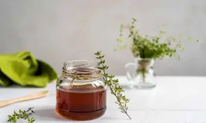 Un bocal de miel ambré, orné de brins de thym frais, évoque les bienfaits naturels de ce trésor doré.