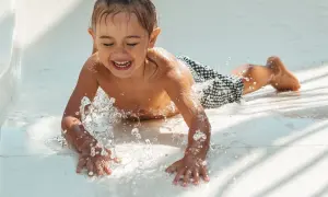 Enfant riant sur un toboggan aquatique, éclaboussures d'eau. Un remède de grand-mère pour l'otite du baigneur pourrait être utile après tant de plaisir !