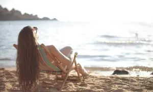 Femme profitant du soleil sur la plage, assise dans une chaise longue, pour faire le plein de vitamine D.