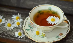Une tasse de thé à la camomille, ornée d'une marguerite, sur une soucoupe décorée. Une belle illustration de la différence entre thé et infusion.