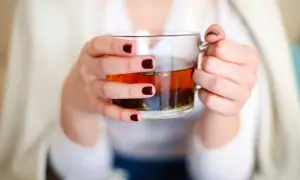 Mains tenant une tasse de thé ambré, se demandant si l'on peut boire des tisanes tous les jours pour un bien-être constant.