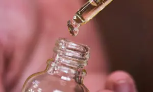 Une goutte d'huile de ricin tombe d'une pipette dans un flacon. Découvrez les bienfaits de l'huile de ricin pour vos cheveux et votre peau.