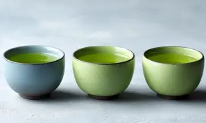 Trois tasses de thé vert vif, une bleue et deux vertes, sur un fond gris. Idéal pour connaître la dose maximale de thé vert par jour.