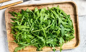 Un plateau en bois déborde de roquette salade fraîche, prête à être dégustée avec des couverts en bois et métal.