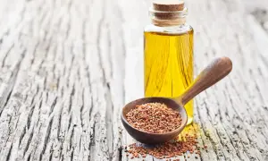 Huile de cameline dorée dans une bouteille, à côté d'une cuillère en bois remplie de graines de cameline. Un remède naturel pour le bien-être des intestins.