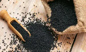 Graine de nigelle : découvrez les nombreuses vertus de ces petites graines noires, ici présentées dans une cuillère en bois et un sac en toile de jute.