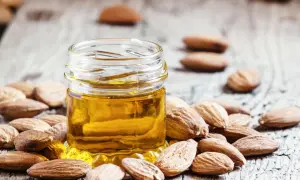 Un petit pot d'huile d'amande douce, entouré d'amandes entières sur fond de bois. Découvrez les bienfaits de l'huile d'amande douce pour la peau.
