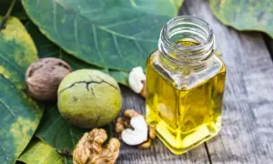 Bouteille d'huile de noix dorée sur des feuilles vertes, entourée de noix entières et décortiquées. Découvrez les bienfaits de l'huile de noix.