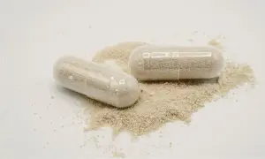 Deux gélules transparentes remplies de poudre beige, posées sur un tas de poudre. Une dose maximale de vitamine D pour votre bien-être.
