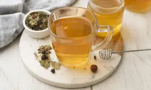 Une tasse de thé aux herbes et au miel, avec un pot de miel et des herbes séchées. Un remède naturel pour un transit trop rapide.