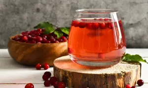 Verre de jus de cranberries, fruit réputé pour aider à prévenir les infections urinaires. Baies rouges dans un bol en bois.