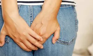 Mains croisées sur un jean, suggérant un inconfort. Apprenez comment se débarrasser des vers intestinaux naturellement.