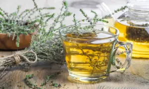 Une tasse de tisane de thym le soir, avec une théière en arrière-plan et des brins de thym frais.