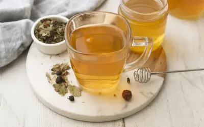 Une tasse de thé aux herbes et au miel, avec un pot de miel et des herbes séchées. Un remède naturel pour un transit trop rapide.