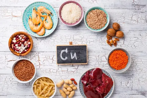 Assiette de crevettes, bols de riz, lentilles, haricots, pâtes, cacahuètes, noix, foie et un tableau noir avec "Cu" pour les cuivre bienfaits.
