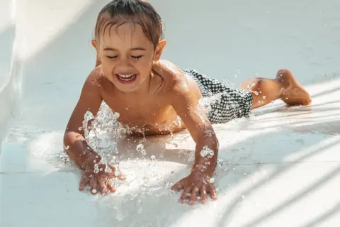 Enfant riant sur un toboggan aquatique, éclaboussures d'eau. Un remède de grand-mère pour l'otite du baigneur pourrait être utile après tant de plaisir !