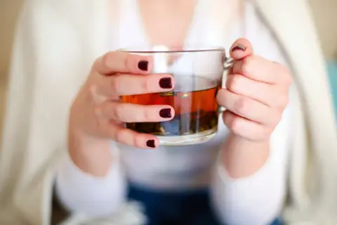 Mains tenant une tasse de thé ambré, se demandant si l'on peut boire des tisanes tous les jours pour un bien-être constant.