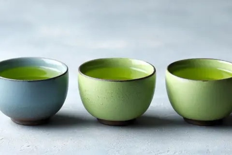 Trois tasses de thé vert vif, une bleue et deux vertes, sur un fond gris. Idéal pour connaître la dose maximale de thé vert par jour.