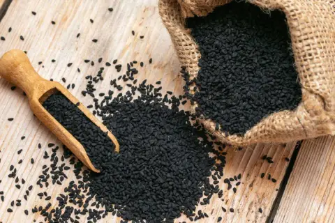 Graine de nigelle : découvrez les nombreuses vertus de ces petites graines noires, ici présentées dans une cuillère en bois et un sac en toile de jute.