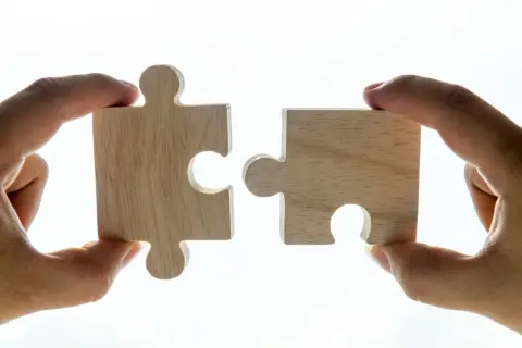 Deux pièces de puzzle en bois, tenues par des mains, symbolisent l'union parfaite de la vitamine D et du magnésium en même temps.