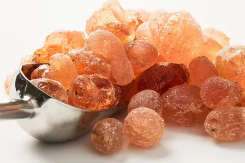 Grains ambrés de gomme arabique, aussi appelée fibre d'acacia, dans une cuillère métallique.