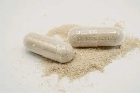 Deux gélules transparentes remplies de poudre beige, posées sur un tas de poudre. Une dose maximale de vitamine D pour votre bien-être.