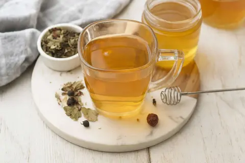 Une tasse de thé aux herbes et au miel, avec un pot de miel et des herbes séchées. Un remède naturel pour un transit trop rapide.