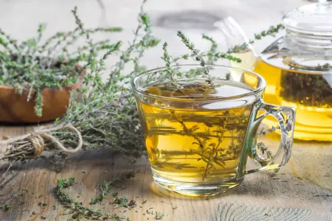 Une tasse de tisane de thym le soir, avec une théière en arrière-plan et des brins de thym frais.