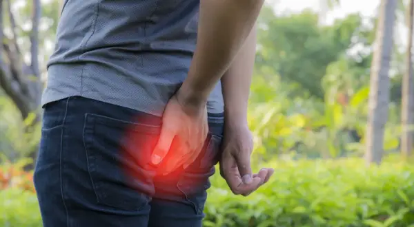Person tenant sa fesse, rougeur indiquant une douleur. Recherche d'un furoncle fessier traitement naturel.