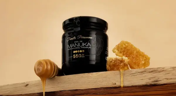 Un pot de miel de Manuka 550+ MGO, avec des rayons de miel et une cuillère à miel dégoulinante. Ce miel de manuka dangereux pour les bactéries, est un trésor de la nature.