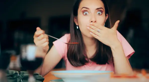 Femme surprise avec une cuillère de soupe, main sur la bouche, comme si elle avait le hoquet persistant.