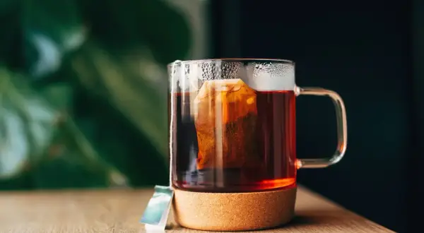 Un moment de détente pour boire du thé après le repas. Une tasse en verre avec un sachet de thé infusant, posée sur un dessous de verre en liège.