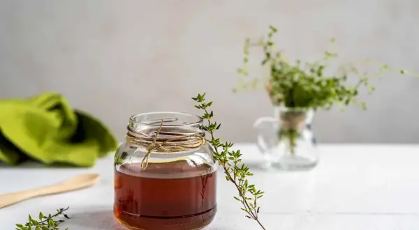 Un bocal de miel ambré, orné de brins de thym frais, évoque les bienfaits naturels de ce trésor doré.