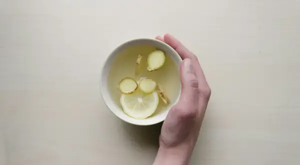 Une main tient un bol de tisane au citron et au gingembre, une boisson réconfortante pour comment prendre soin de son foie.