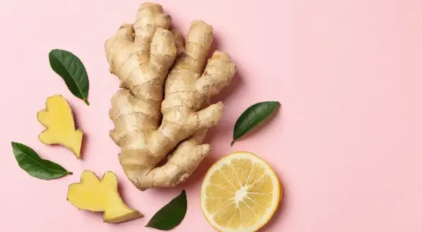 Gingembre anti inflammatoire, citron et feuilles vertes sur fond rose. Un remède naturel pour le bien-être.