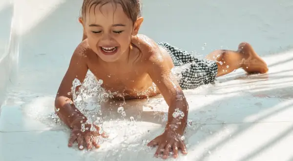 Enfant riant sur un toboggan aquatique, éclaboussures d'eau. Un remède de grand-mère pour l'otite du baigneur pourrait être utile après tant de plaisir !