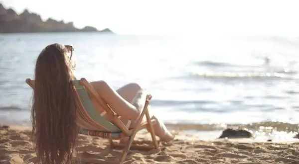Femme profitant du soleil sur la plage, assise dans une chaise longue, pour faire le plein de vitamine D.