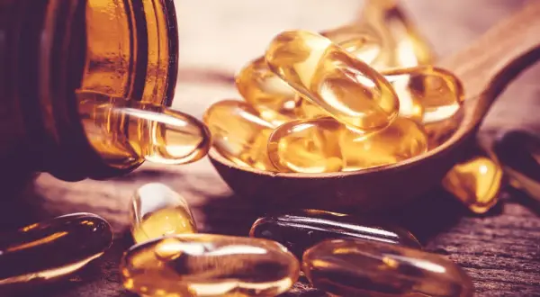 Gélules dorées sur une cuillère en bois, évoquant la vitamine D sans soleil.