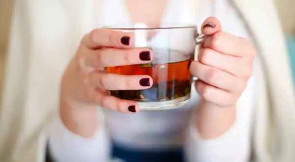 Mains tenant une tasse de thé ambré, se demandant si l'on peut boire des tisanes tous les jours pour un bien-être constant.