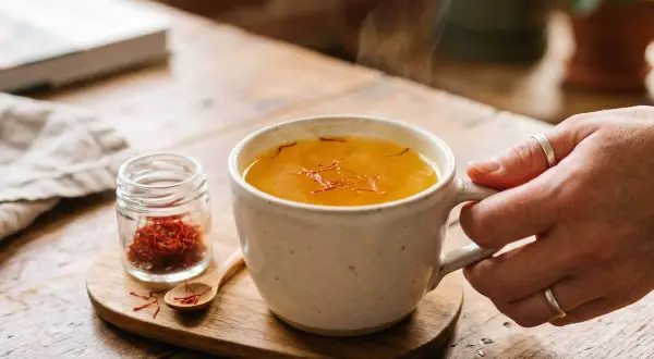 Une tasse de thé fumant au safran, avec un petit pot de pistils. Attention, le safran peut présenter un danger s'il est consommé en excès.
