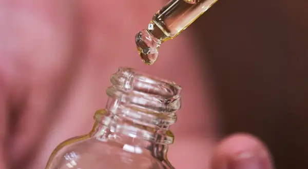 Une goutte d'huile de ricin tombe d'une pipette dans un flacon. Découvrez les bienfaits de l'huile de ricin pour vos cheveux et votre peau.