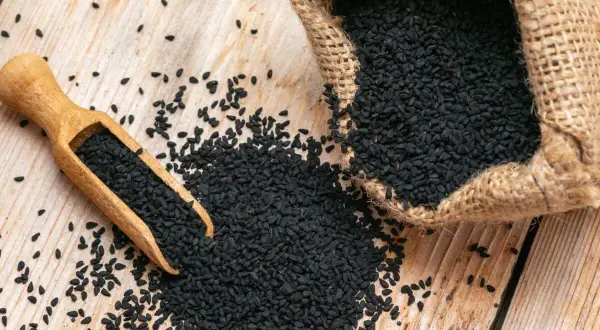 Graine de nigelle : découvrez les nombreuses vertus de ces petites graines noires, ici présentées dans une cuillère en bois et un sac en toile de jute.