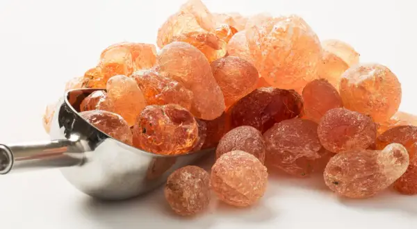 Grains ambrés de gomme arabique, aussi appelée fibre d'acacia, dans une cuillère métallique.