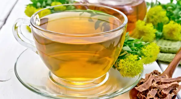 Une tasse de thé ambré, des fleurs de rhodiola et des racines séchées. Attention, la rhodiola peut présenter un danger si mal utilisée.