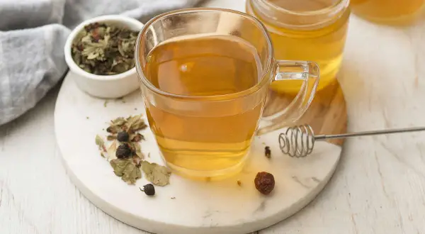 Une tasse de thé aux herbes et au miel, avec un pot de miel et des herbes séchées. Un remède naturel pour un transit trop rapide.