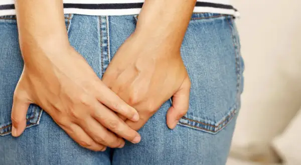Mains croisées sur un jean, suggérant un inconfort. Apprenez comment se débarrasser des vers intestinaux naturellement.